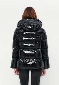 Svart puffjakke med en blank, polstret overflate, med hette og horisontale sømmer. Ermene er litt utvidet, noe som gir varme.