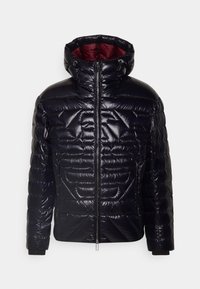 Pohodlná černá bunda s vysokým límcem a zipovým zapínáním. Znaky lesklé textury a šikmého prošívání ve tvaru diamantu. Vnitřek je podšitý červenou látkou.