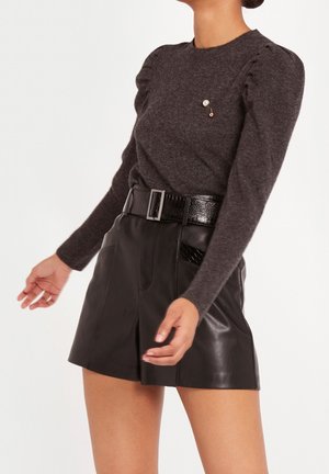 Suéter de lana gris oscuro con hombros abullonados y un pin decorativo, combinado con pantalones cortos de piel negra de cintura alta con una textura brillante y bolsillos.