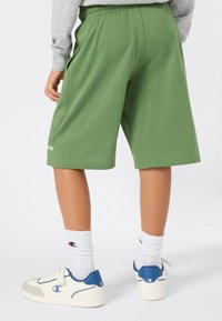 Groene katoenen shorts met een elastische tailleband en zijzakken. Een klein "Champion"-logo staat op de onderste linkerbenen.