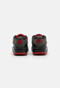 Nike Air sneakers har en grå og svart overdel med røde detaljer, en polstret krage og et teksturert design. Gummisålen er rød.