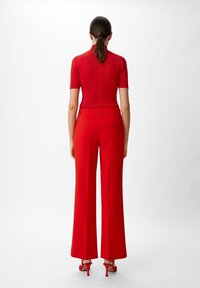 Top rojo ajustado de manga corta combinado con pantalones rojos de talle alto y pierna ancha. Textura suave, detalles mínimos y tacones rojos a juego.