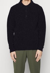 Dunkelgrauer Pullover mit weicher Textur, Kragen-Design, Drei-Knopf-Leiste und langen Ärmeln. Getragen mit olivgrünen Hosen.