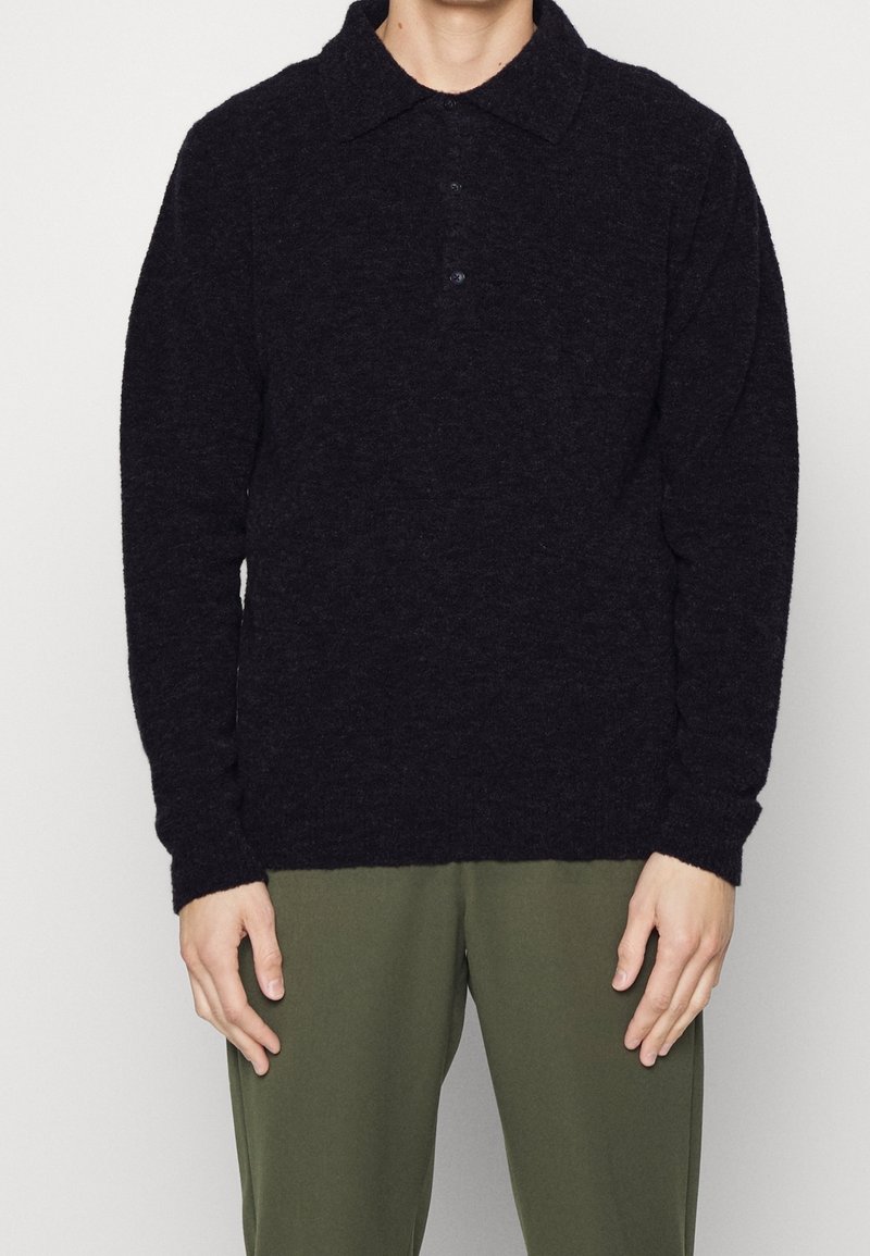 Dunkelgrauer Pullover mit weicher Textur, Kragen-Design, Drei-Knopf-Leiste und langen Ärmeln. Getragen mit olivgrünen Hosen.