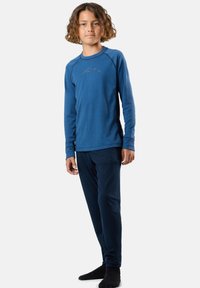 Top blu lungo a maniche, con una texture a costine e grafica di montagna, abbinato a pantaloni blu scuri. Entrambi i capi hanno una vestibilità comoda e un materiale morbido.
