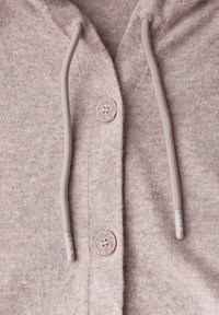 Sweat à capuche brun clair en tissu texturé, avec une fermeture à bouton et des cordons de serrage contrastants avec des embouts marqués.