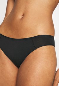 Fekete pamut bikini alsó, sima textúrával, alacsony derékszámmal és minimális varrással a derékrészen és a lábnyílásoknál.