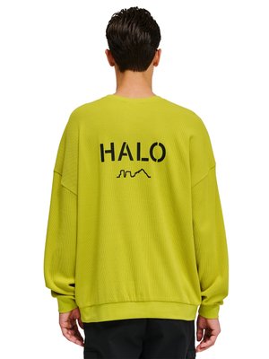 Man draagt een losse limegroene trui met "HALO" en een klein skyline-ontwerp in het zwart op de achterkant gedrukt.