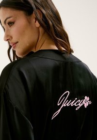 Melnas satīna halāts ar rozā izšuvumu un ziedu motīvu uz muguras. Gluda tekstūra un klasiskas apkakles dizains.