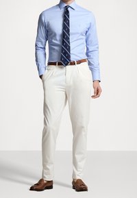 Camisa de manga larga azul claro, corbata azul marino con patrón de anclas, pantalones color crema, mocasines de cuero marrón con borlas y cinturón marrón.