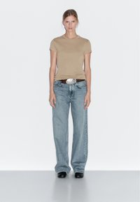 Béžové přiléhavé tričko, spárované se světle modrými širokými džínami, doplněné hnědým páskem s velkou kovovou sponou a černou obuví.