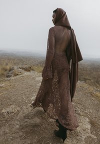 Hnedá čipkovaná šaty s dlhými, rozšírenými rukávmi, otvoreným chrbtom a vrstveným šálom. Tkanina má kvetinové vzory a plynulý siluetu.