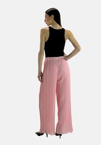 Flessige roze geplooide broek met een elastische tailleband, gecombineerd met een zwart mouwloos topje. Gladde textuur en wijd uitlopende pijpen, enkel-lang.
