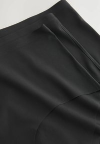 Mustast kangast, millel on sile tekstuur ja kihiline disain. Äärtes on korrektselt õmmeldud peened õmblused.