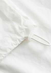 Gros plan sur un tissu blanc avec une couture cousue et une boucle de cordon élastique maintenue par un arrêt en plastique transparent.
