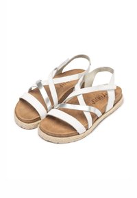 White sandals with crossed straps featuring a metallic silver accent. Cork-like footbed and textured sole for grip. Adjustable heel strap.
