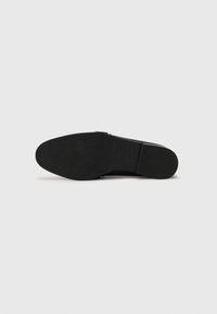 Black shoe sole with a smooth, flat surface and subtle texture. Features a rounded shape and minimal detailing, made from durable material.