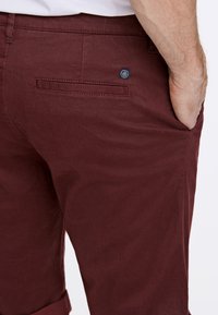 Burgundy chinos med en texturerad tygkvalitet, slim fit och en bakficka med ett märkesplagg. Vikta fållar ger en skräddarsydd känsla.
