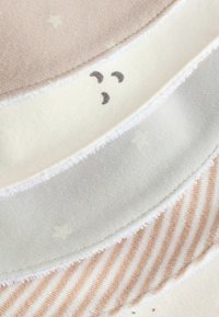 Zachte stofstukken in beige, crème en lichtgrijs. Met sterren en strepen, met gestructureerde randen en lichte patronen.