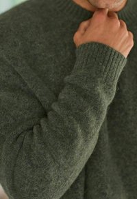 Pull en maille vert foncé avec des poignets et un col côtelés, présentant un tissu doux et texturé, affiché sur un fond neutre.