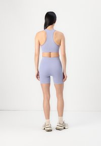 Light purple ribbed crop top with racerback design paired with matching high-waisted shorts, both featuring a smooth texture. Athletic sneakers worn.