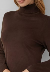 Brauner Rollkragenpullover aus weichem Strickstoff. Er bietet eine enganliegende Passform, lange Ärmel und einen nahtlosen gerippten Kragen für zusätzlichen Komfort.
