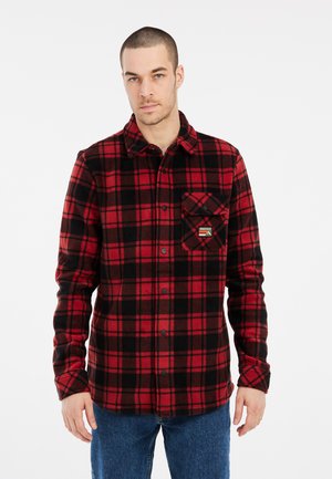 Rood en zwart geblokt flanellen shirt met een knoopsluiting, een enkele borstzak en een zachte textuur. Draag het over een donker shirt en blauwe spijkerbroek.