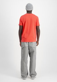 Camiseta de algodón roja con mangas cortas, combinada con pantalones cargo grises que tienen bolsillos laterales y un ajuste relajado. Acentuada por un gorro de punto gris.
