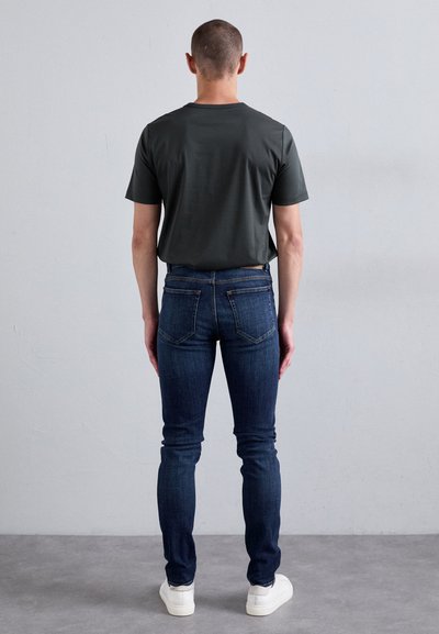Tricou scurt de culoare gri închis, cu mânecă scurtă, purtat cu blugi slim-fit de culoare albastră închis, asortați cu adidași albi. Textile netede, cu detalii minime de cusătură.