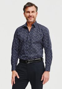 Granatowa koszula z motywem kwiatowym w małe białe i fioletowe kropki. Długie rękawy, kołnierzyk zapinany na guziki oraz proste wykończenie. Noszony czarny pasek.