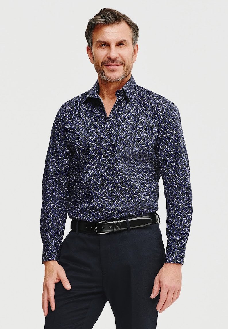 Granatowa koszula z motywem kwiatowym w małe białe i fioletowe kropki. Długie rękawy, kołnierzyk zapinany na guziki oraz proste wykończenie. Noszony czarny pasek.