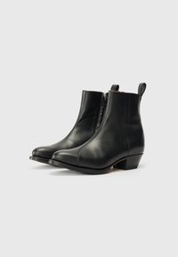 Botas de tobillo de cuero negro con punta ligeramente afilada, cremallera lateral y tacón bajo en bloque; textura suave y diseño minimalista.