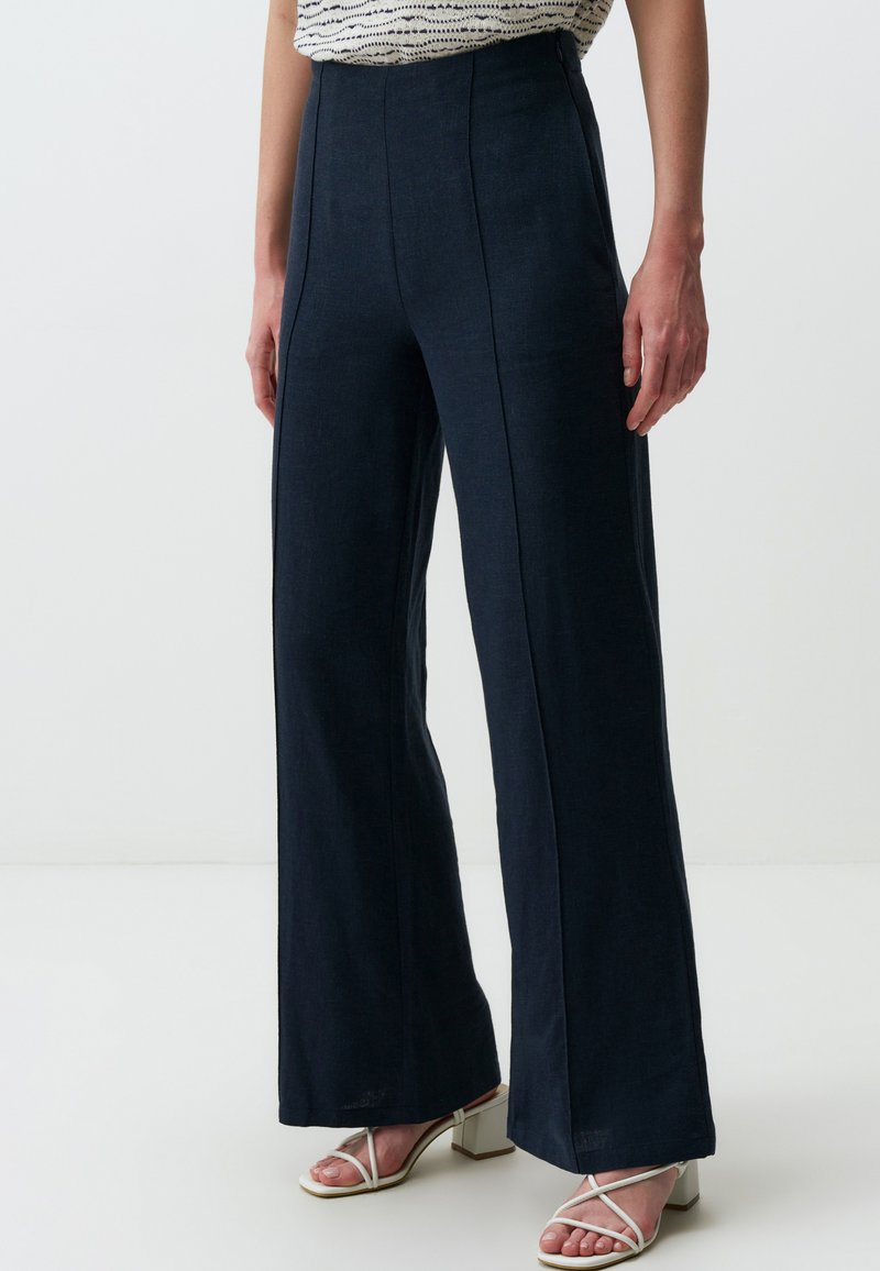 Spodnie o szerokich nogawkach w ciemnonawiwowym kolorze z gładkiego materiału, z pionowymi szwami dla dodatkowej struktury. Połączone z sandałami na obcasie z paskami.