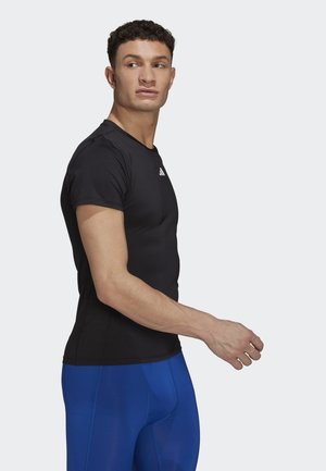 Camiseta atlética negra de manga corta combinada con leggings azules, con un diseño ajustado y un pequeño logo blanco en el frente.