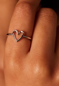 Zilveren ring met een open hartontwerp. De band is glad en strak, liggend op een hand met een gestructureerde huidtextuur.