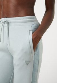 Gaiši zili sporta bikses ar teksturētu rakstu gar sānu. Iekļauj pievilkšanas jostu, sānu kabatas un mazu izšūtu logo uz augšstilba.