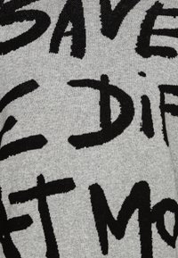 Tissu gris avec des motifs de texte noirs audacieux, présentant de grandes lettres irrégulières dans un style décontracté et peint à la main.