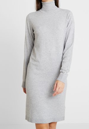 Frau trägt ein hellgraues, langärmliges, knielanges Strickkleid mit Rollkragen und gerippten Bündchen sowie Saum.