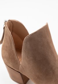 Bruine suède enkellaars met een ronde neus, korte rits en een houten blokhak. Eenvoudige naaddetails langs de randen.