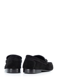 Mocassins en velours noir avec un petit talon, possédant un bout arrondi et des surpiqûres décoratives sur les côtés. Accents en cuir lisse près de l'ouverture.