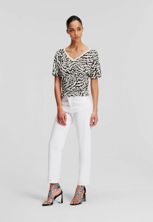 Top corto de manga corta con un patrón abstracto en blanco y negro, combinado con jeans blancos de cintura alta y sandalias de tacón con tiras en blanco y negro.