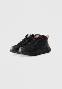 Une paire de chaussures de sport New Balance noires avec un logo orange et une poignée, des lacets noirs avec des fermetures à clip, sur un fond blanc.
