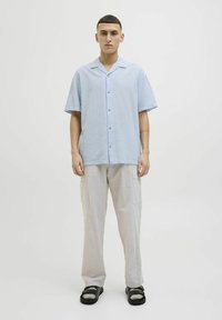 Camisa de botones de manga corta azul claro con cuello, combinada con pantalones cargo grises claros. Se llevan sandalias negras con un acento metálico.