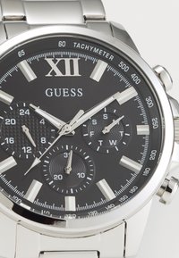 Montre en acier inoxydable avec un cadran noir. Comprend des index d'heure en argent, une échelle tachymétrique et trois sous-cadrans avec des motifs texturés.