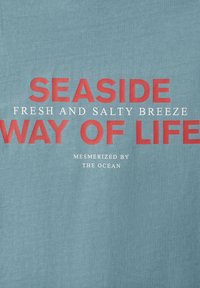 Tissu bleu avec texte rouge et blanc disant « Mode de vie en bord de mer, brise fraîche et salée, fasciné par l'océan. »