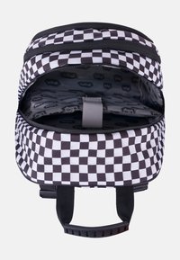Zaino a scacchi in bianco e nero con due cerniere, un interno foderato e una tracolla grigia per fissare il contenuto; visibile la texture del tessuto.