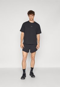 Ensemble de t-shirt et shorts de sport noir, fabriqué en tissu léger. Comprend un col rond, des manches courtes et un logo discret sur la poitrine.