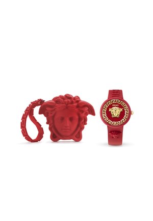 Rood rubberen horloge met een gouden embleem en Grieks sleutelmotief, vergezeld van een rode gedraaide armband en een hoofdvormige kast.