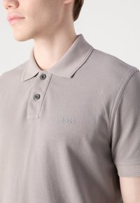 Polo tričko v světlé šedé barvě z bavlněné směsi s texturovaným povrchem. Má klasický límec, dvě knoflíky a decentní logo 'BOSS' na hrudi.