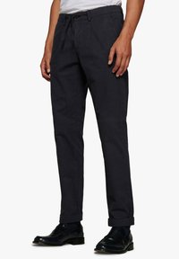Chinos azul marino oscuro de tela texturizada. Cuentan con una cintura ajustada, trabillas para cinturón y puños enrollados. Estilizados con mocasines negros.